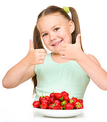 Image showing Happy little girl is eating strawberries