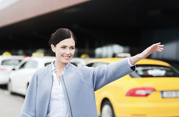 Image showing smiling young woman waving hand and catching taxi