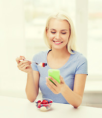 Image showing woman with smartphone eating fruits at home