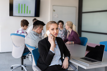 Image showing business woman speeking on phone at office with team on meeting 