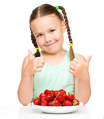 Image showing Happy little girl is eating strawberries