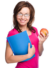 Image showing Young student girl is holding book and apple