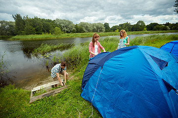 Image showing group of smiling friends setting up tent outdoors