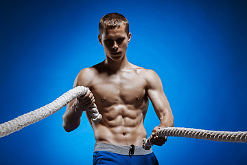 Image showing Fit young man with beautiful torso and a rope on blue background