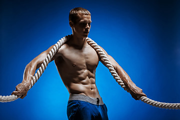 Image showing Fit young man with beautiful torso and a rope on blue background