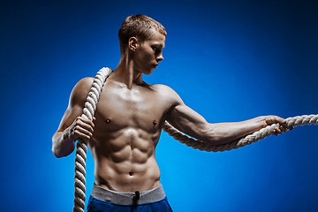 Image showing Fit young man with beautiful torso and a rope on blue background