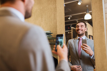 Image showing man in suit taking mirror selfie at clothing store