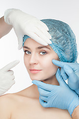 Image showing Plastic surgery concept. Doctor hands in gloves touching the beautiful woman face on white