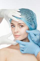 Image showing Plastic surgery concept. Doctor hands in gloves touching the beautiful woman face on white