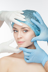 Image showing Plastic surgery concept. Doctor hands in gloves touching the beautiful woman face on white