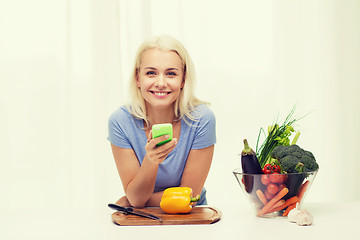 Image showing smiling woman with smartphone cooking vegetables