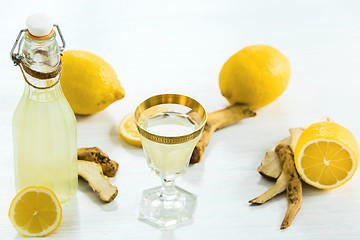 Image showing Home ginger tincture in a glass and fresh lemons on the white wooden background