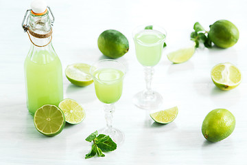 Image showing Home lime liquor in a glass and fresh lemons and limes on the white wooden background