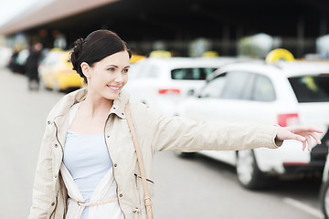 Image showing smiling young woman waving hand and catching taxi