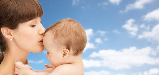 Image showing happy mother kissing baby boy over sky background