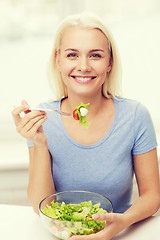 Image showing smiling young woman eating salad at home