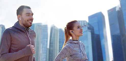 Image showing happy couple with earphones running in city