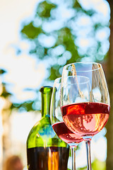 Image showing two glasses filled with red wine and bottle in background