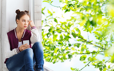 Image showing teenage girl sitting on windowsill with smartphone