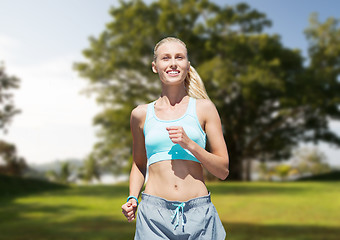 Image showing smiling young woman running or jogging over park