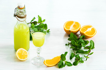 Image showing Home orange liquor in a glass and fresh oranges on the white wooden background