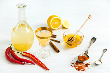 Image showing Home red pepper tincture in a glass and fresh lemons on the white wooden background