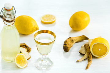 Image showing Home ginger tincture in a glass and fresh lemons on the white wooden background