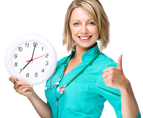 Image showing Young lady doctor is holding clock showing seven