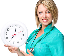 Image showing Young lady doctor is holding clock showing seven