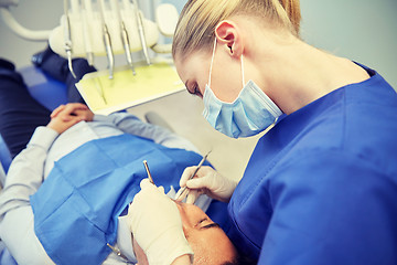 Image showing female dentist in mask checking male patient teeth