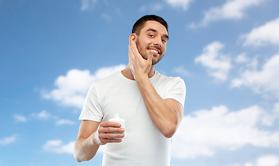 Image showing happy young man applying cream or lotion to face