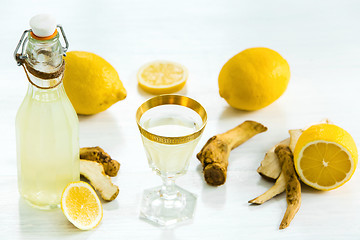 Image showing Home ginger tincture in a glass and fresh lemons on the white wooden background