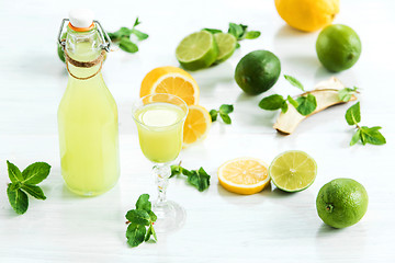 Image showing Home lime liquor in a glass and fresh lemons, limes on the white wooden background