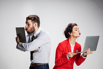 Image showing The young businessman and businesswoman with laptops kissing screens on gray background