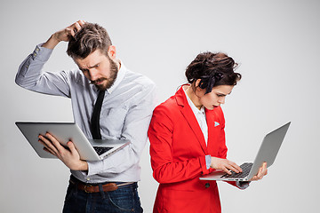 Image showing The young businessman and businesswoman with laptops communicating on gray background