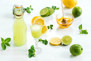 Image showing Home lime liquor in a glass and fresh lemons, limes on the white wooden background