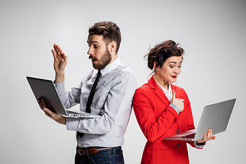 Image showing The young businessman and businesswoman with laptops communicating on gray background