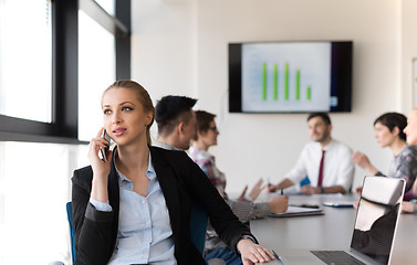 Image showing business woman speeking on phone at office with team on meeting 