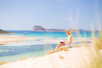 Image showing Woman reading book, enjoying sun on beach.