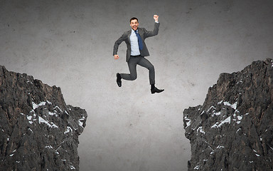 Image showing happy smiling businessman jumping between rocks