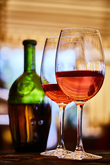 Image showing two glasses filled with red wine and bottle in background