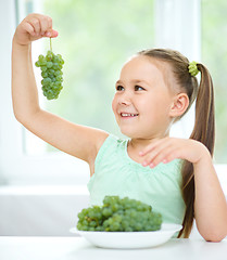 Image showing Cute little girl is looking at green grapes