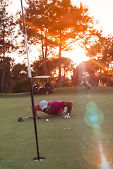 Image showing golf player blowing ball in hole with sunset in background