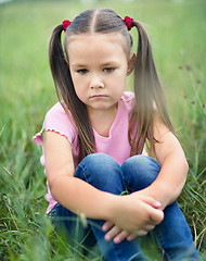 Image showing Sad little girl is sitting on green grass