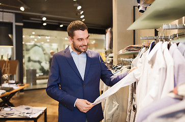 Image showing happy young man choosing clothes in clothing store