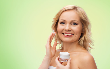 Image showing happy woman applying cream to her face