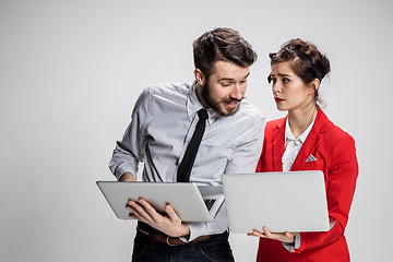 Image showing The young businessman and businesswoman with laptops communicating on gray background