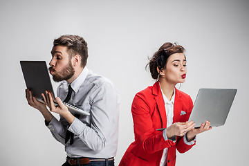 Image showing The young businessman and businesswoman with laptops kissing screens on gray background