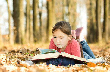 Image showing Little girl is reading a book outdoors