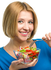 Image showing Young attractive woman is eating salad using fork
